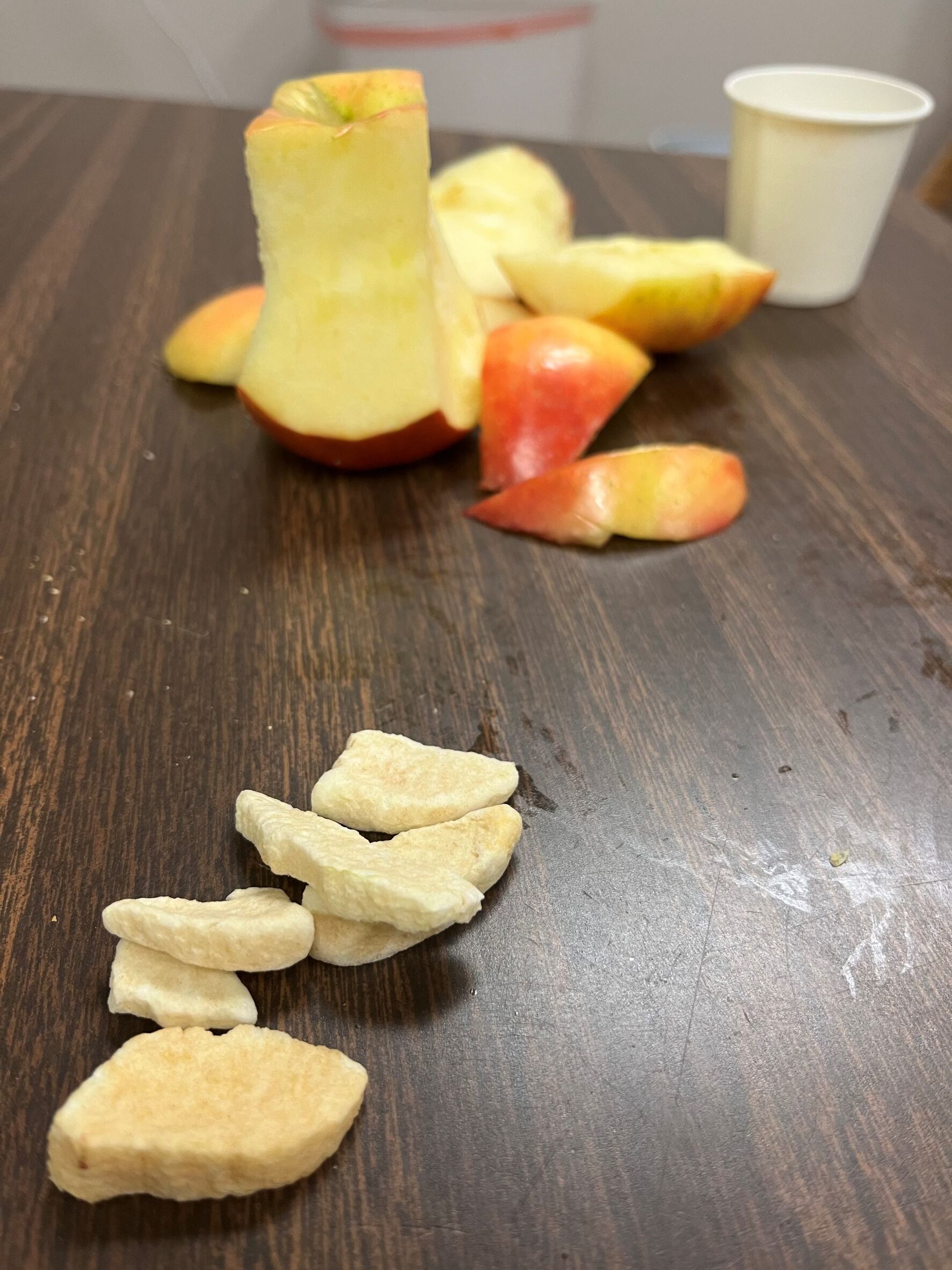 An apple cut into slices next to dehydrated apple slices on a table.